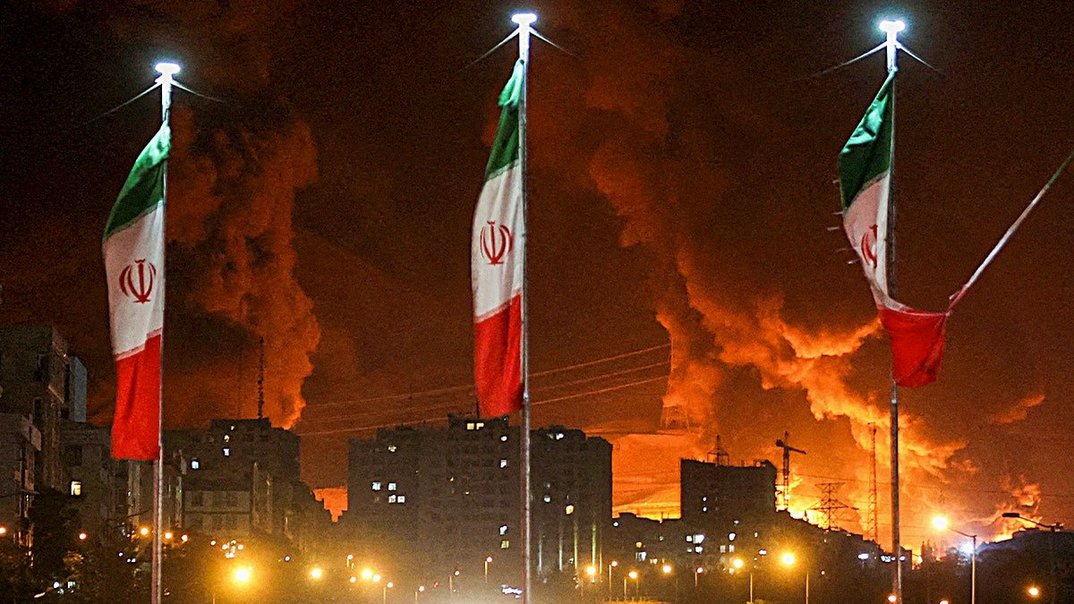 Iranian flags flying with fire and smoke rising from Sharan Oil depot after Israeli attack