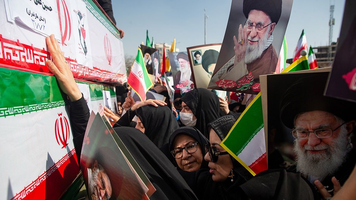 Mourners reaching out to touch coffins while holding pictures of Ayatollah Ali Khamenei during a funeral in Isfahan.