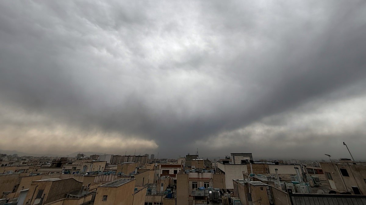Plumes of dark smoke rising from an oil facility in Tehran, Iran, merging with a cloudy sky.