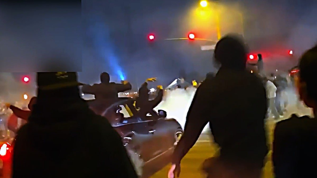 A car with people hanging out of it drifts through an intersection as people look on.