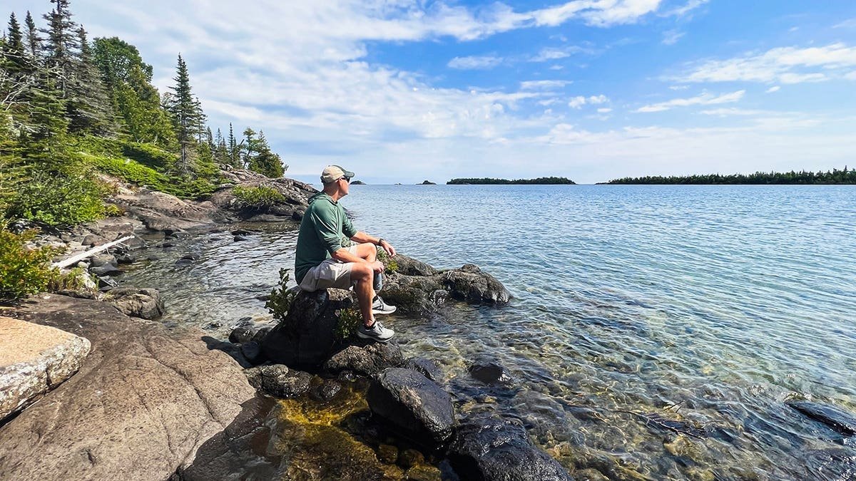 A man sitting on a large rock overlooking Lake Superior at Isle Royale National Park in Michigan