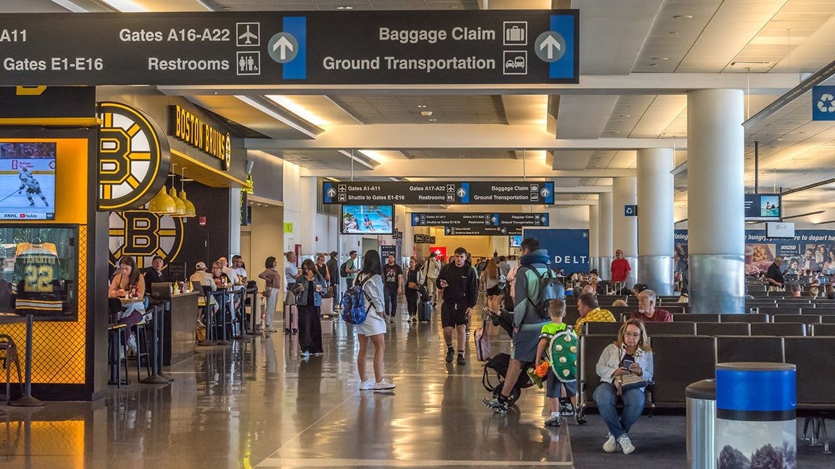 Travelers seated and standing inside a crowded waiting room at Logan International Airport in Boston