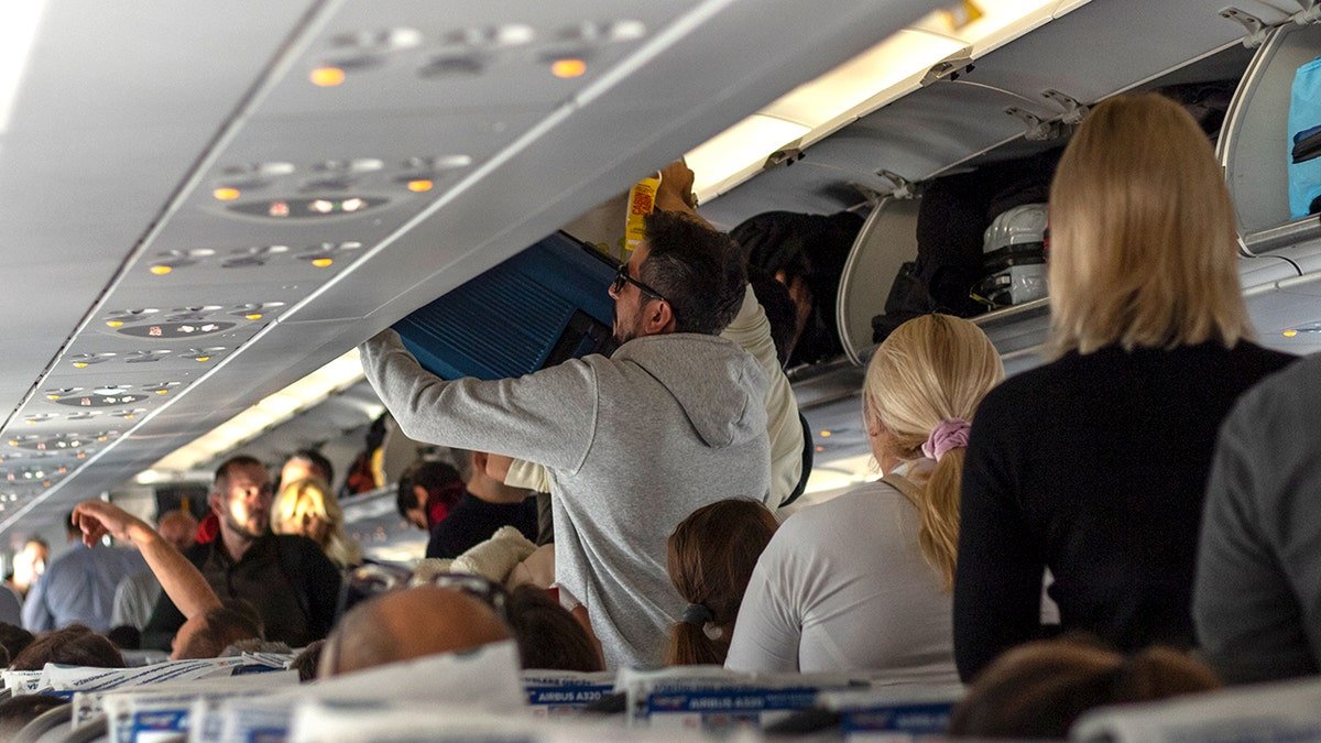 Passengers stacking baggage on luggage racks inside an airplane cabin