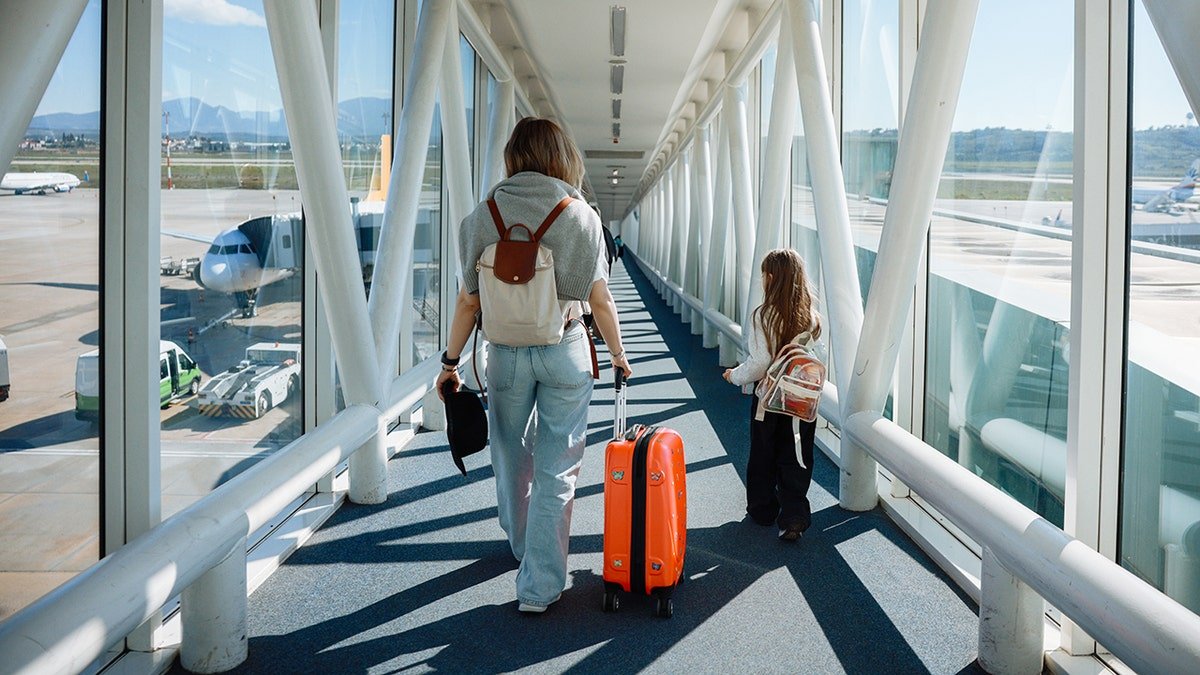 Mother and daughter walking on jet bridge with backpacks and suitcases at airport