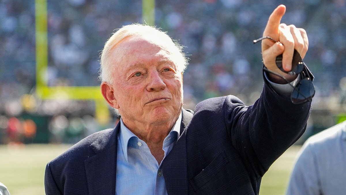 Dallas Cowboys owner Jerry Jones standing on the field pointing to the crowd at MetLife Stadium.