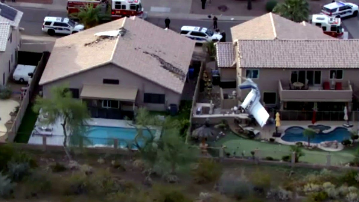 damaged roof of home and small plane wreckage in residential backyard