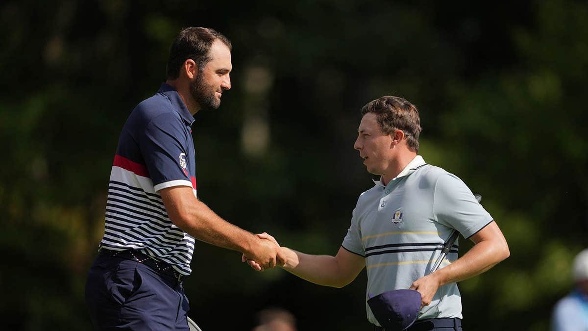 Scottie Scheffler and Matt Fitzpatrick shaking hands on the 15th green at Bethpage State Park Golf Course.