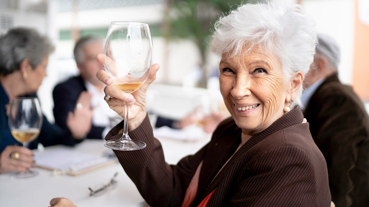Smiling senior woman holding a wine glass with friends behind her in a dining setting