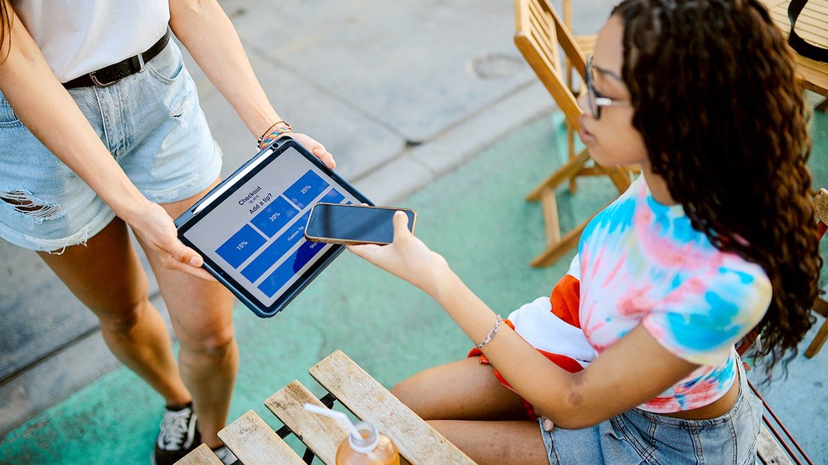 A young woman using a tablet to leave a tip at an outdoor cafe in Venice, Calif.