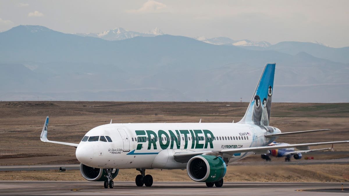 A Frontier Airlines flight taxis at Denver International Airport with the Colorado Rocky Mountains in the background