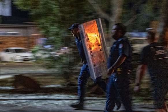 A police officer carries a large riot shield.