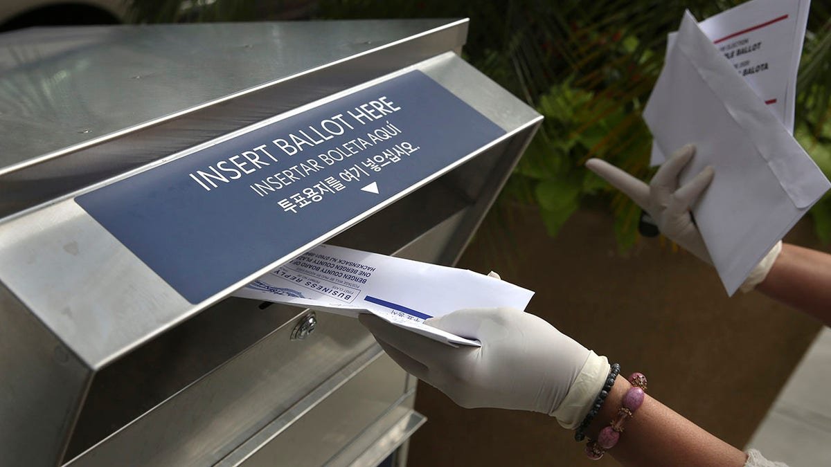 A woman wearing gloves drops off a mail-in ballot at a drop box in Hackensack New Jersey