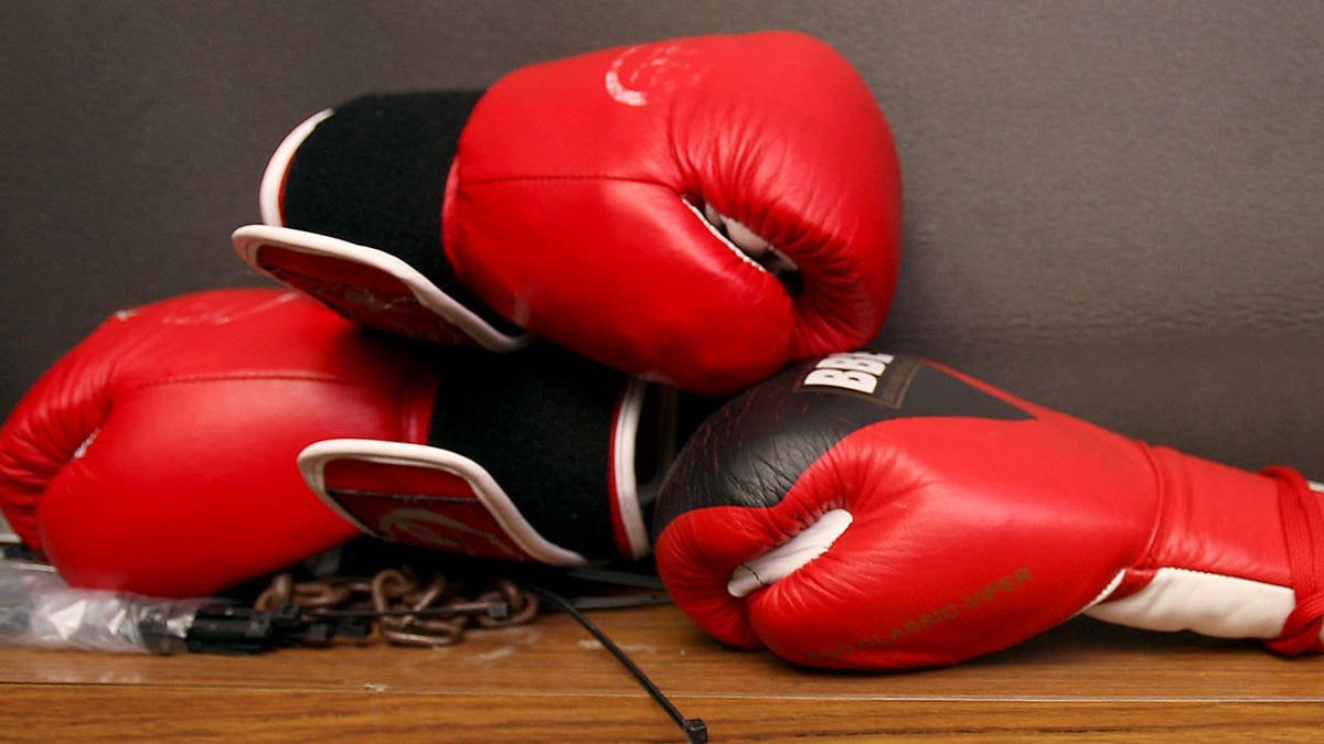 Three red BBE boxing gloves sitting on a surface.