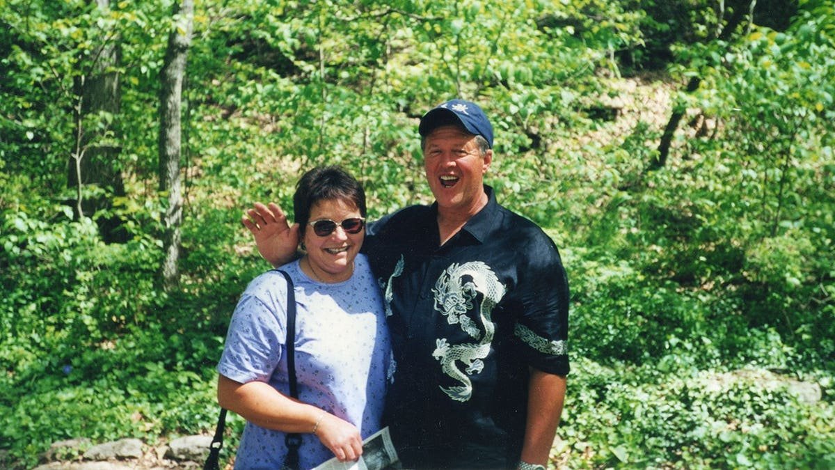 Deb Proctor and Jeff Walton standing in a forest and smiling together.