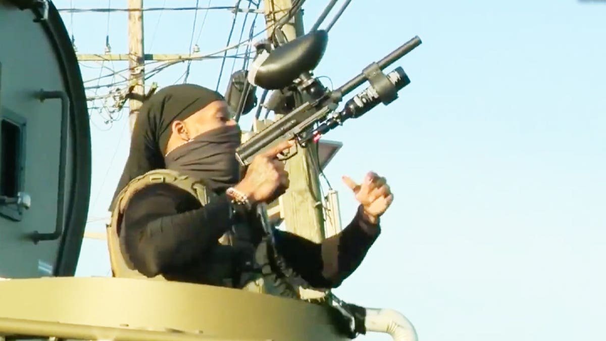 An ICE agent wields a paintball gun from atop an armored vehicle
