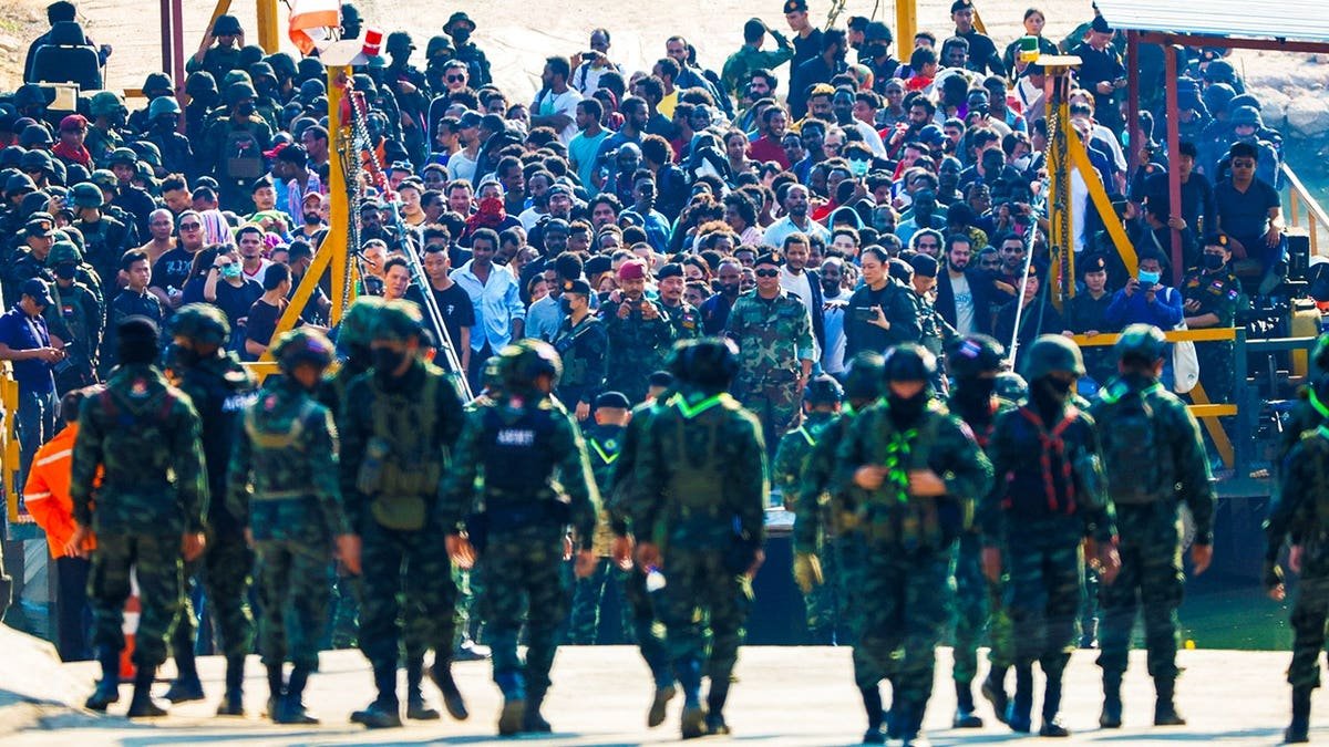 Multinational victims of scam centers stand in a crowd near an army