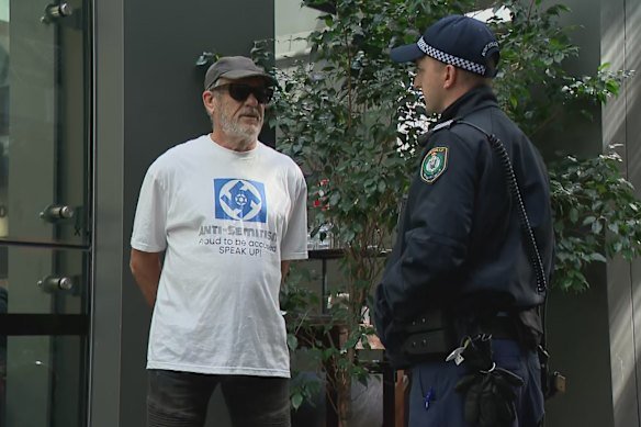 Police outside the building holding the Royal Commission into Antisemitism and Social Cohesion in the Sydney CBD speak to a man wearing an antisemitic T-shirt.