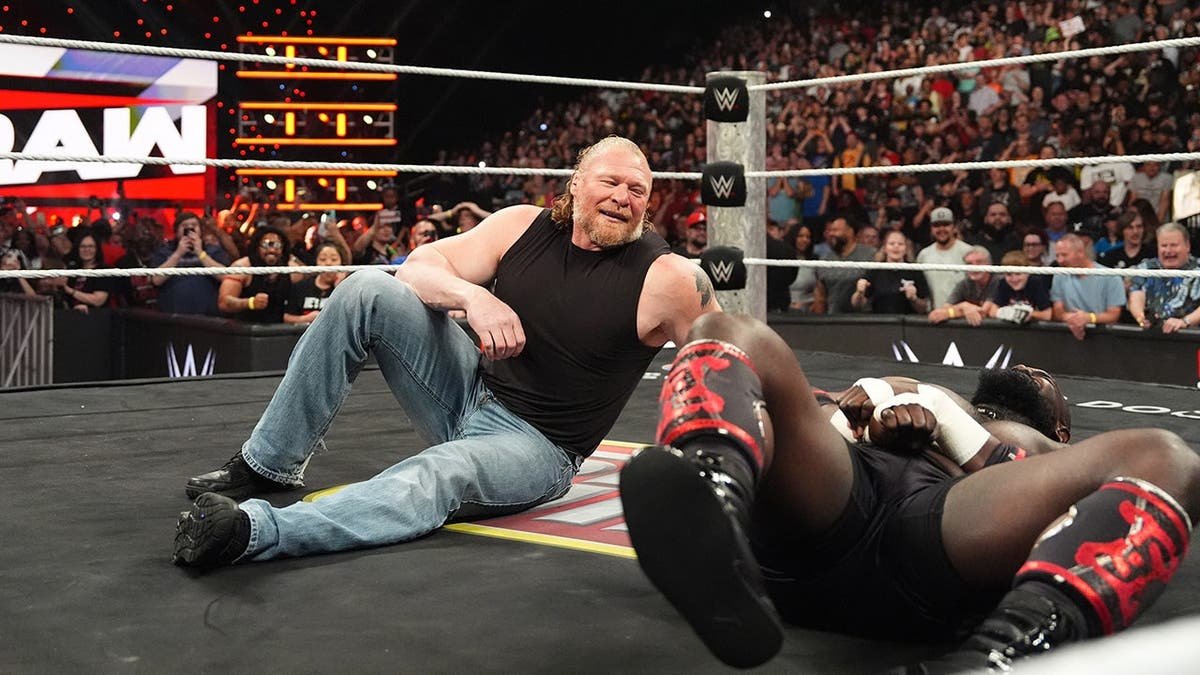 Brock Lesnar smiling while looking at Oba Femi lying on the mat during wrestling match