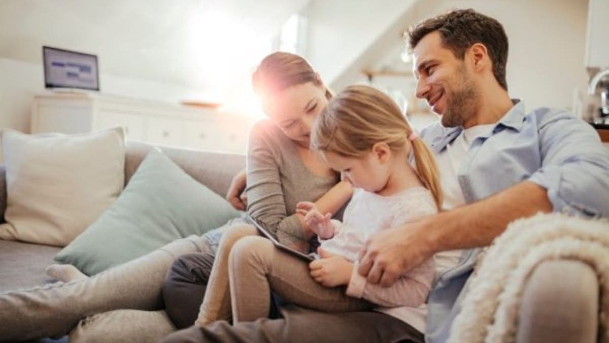 Parents sitting with their young daughter using a tablet on a couch at home