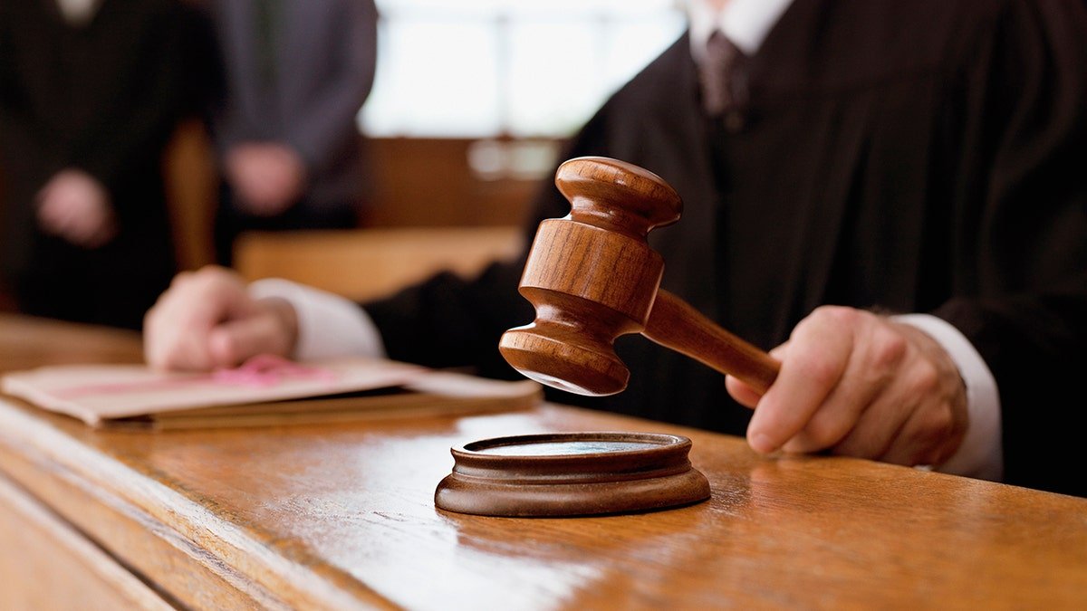 Close-up of a judge holding a wooden gavel above a sound block in a courtroom.