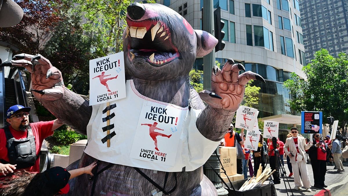 Protesters holding Kick ICE Out signs on an inflatable rat outside SoFi Stadium