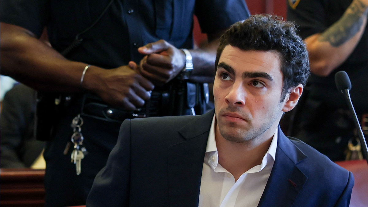 Luigi Mangione leaning to the side in Manhattan Supreme Court with an officer standing behind him