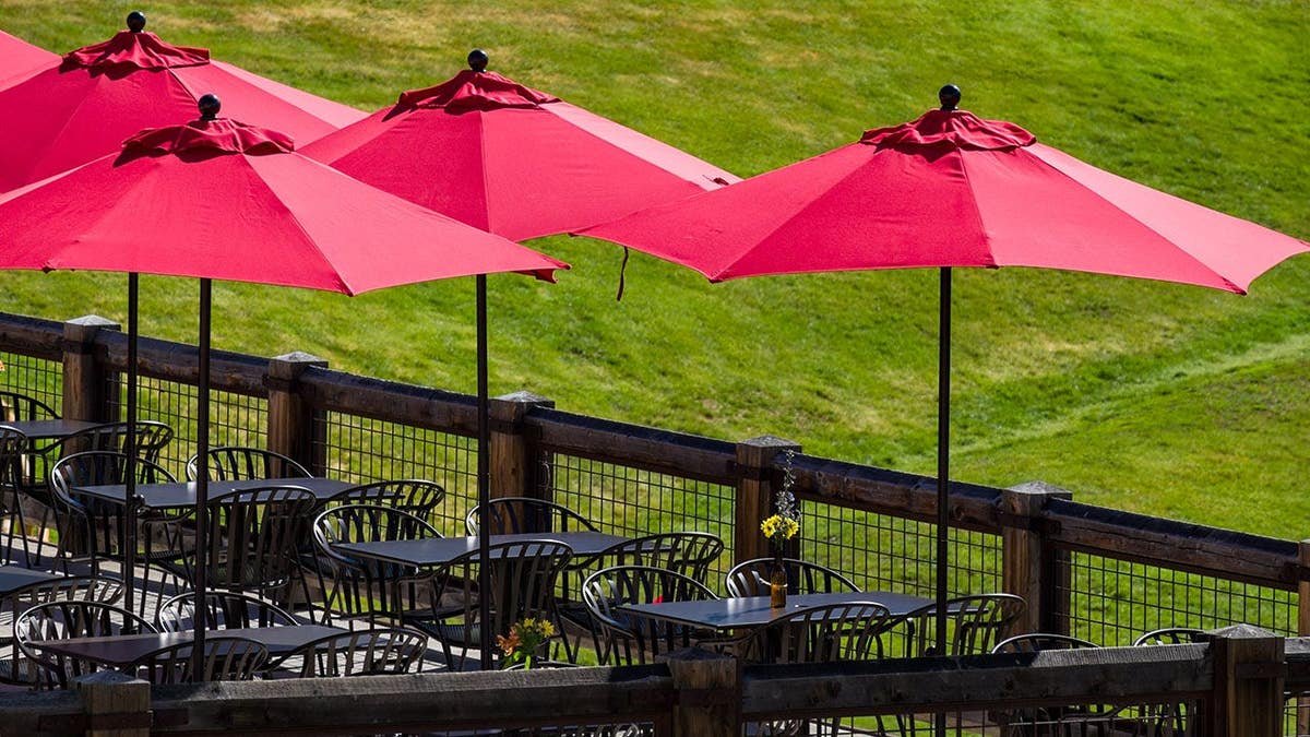 Red umbrellas shading outdoor tables on a patio with green grass
