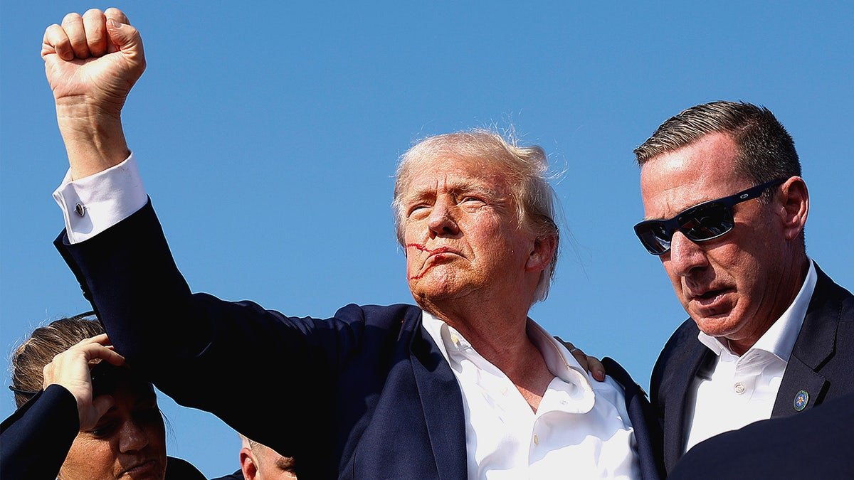 Donald Trump raising his fist while being escorted offstage by Secret Service agents