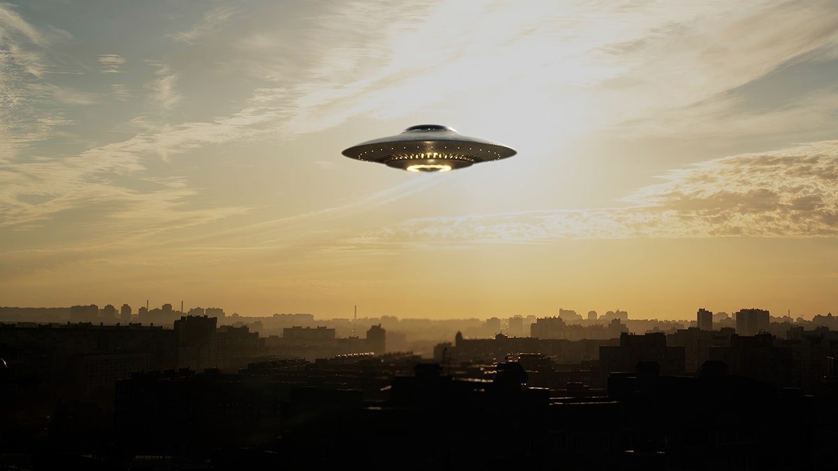 A UFO hovering over land in a cloudy sky.