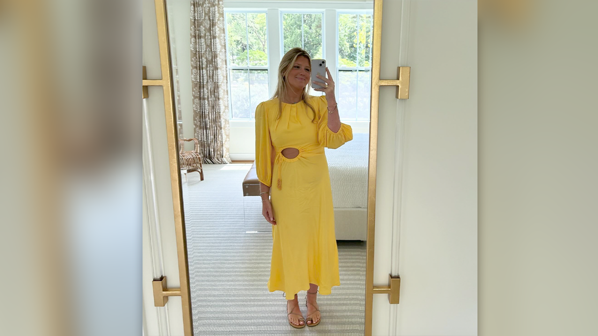 Whitney Robeson wearing a yellow dress and holding her phone for a selfie in a mirror