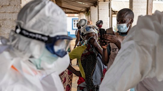 Health workers wearing protective suits prepare for Ebola response operations as residents gather outside a hospital in Mongbwalu, Democratic Republic of the Congo.