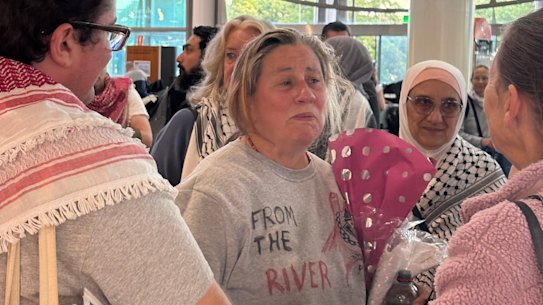 Flotilla activist Helen O’Sullivan (centre) arrives in Brisbane on Monday morning, greeted by about 20 family members and friends including Liam Parry (left), the first person charged under new Queensland hate speech laws.