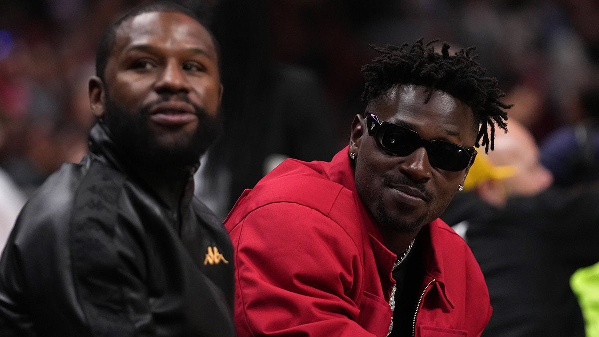Floyd Mayweather Jr. sitting with Antonio Brown during a basketball game.