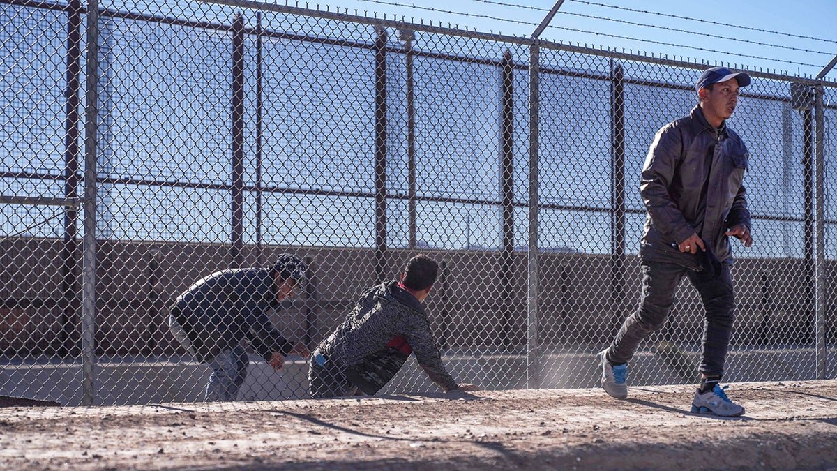 Migrants crossing through a hole in a fence at the Texas border near El Paso