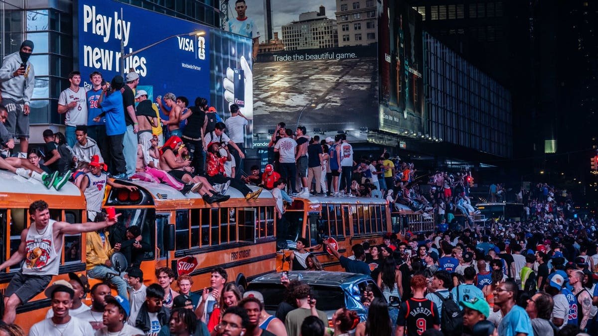 New York Knicks fans climb on buses as they celebrate after they win the NBA Finals in Times Square on June 14, 2026 in New York City.