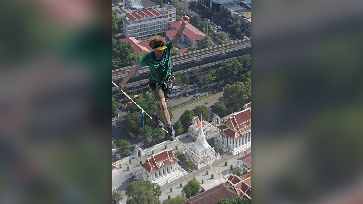 Daredevil Andy Lewis in a green T-shirt and khaki shorts crosses a highline above Bangkok, Thailand