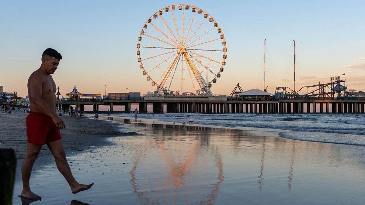 A man walks past a Ferris wheel's reflection on the beach at sunset in Atlantic City, New Jersey.