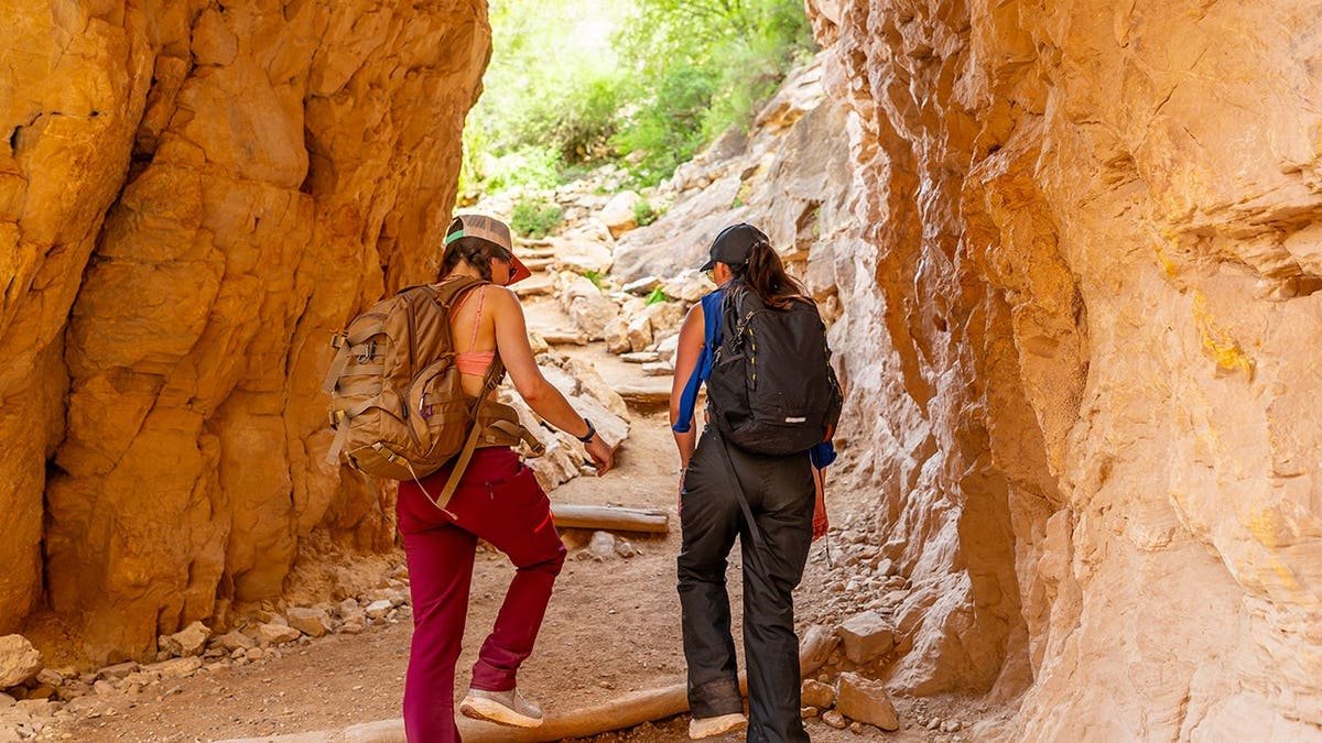 Two women hiking up Bright Angel Trail through a sandstone tunnel in Grand Canyon National Park