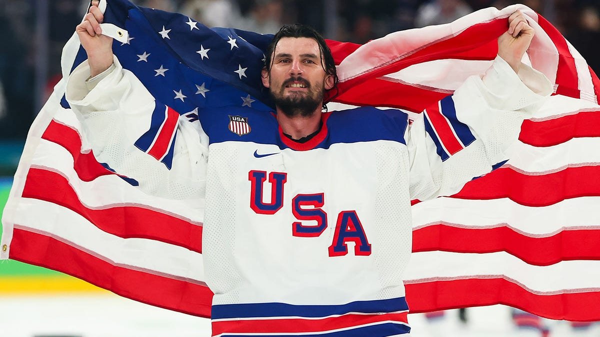 Connor Hellebuyck holding up a flag celebrating on ice hockey rink