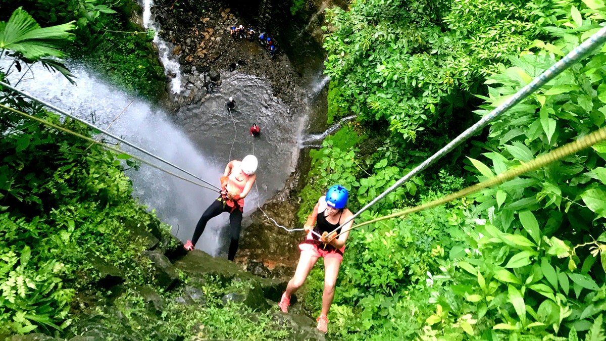 Two people rock climbing over a waterfall in a Costa Rica rainforest