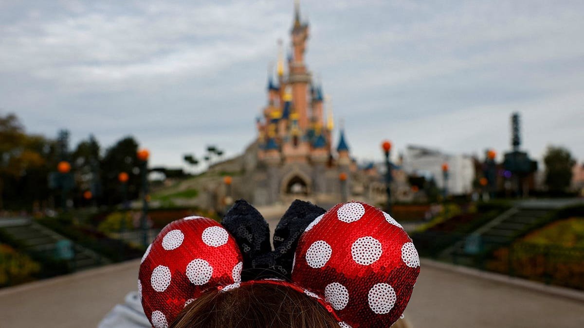 A visitor wearing Mickey and Minnie Mouse ears standing in front of the Sleeping Beauty castle at Disneyland Paris