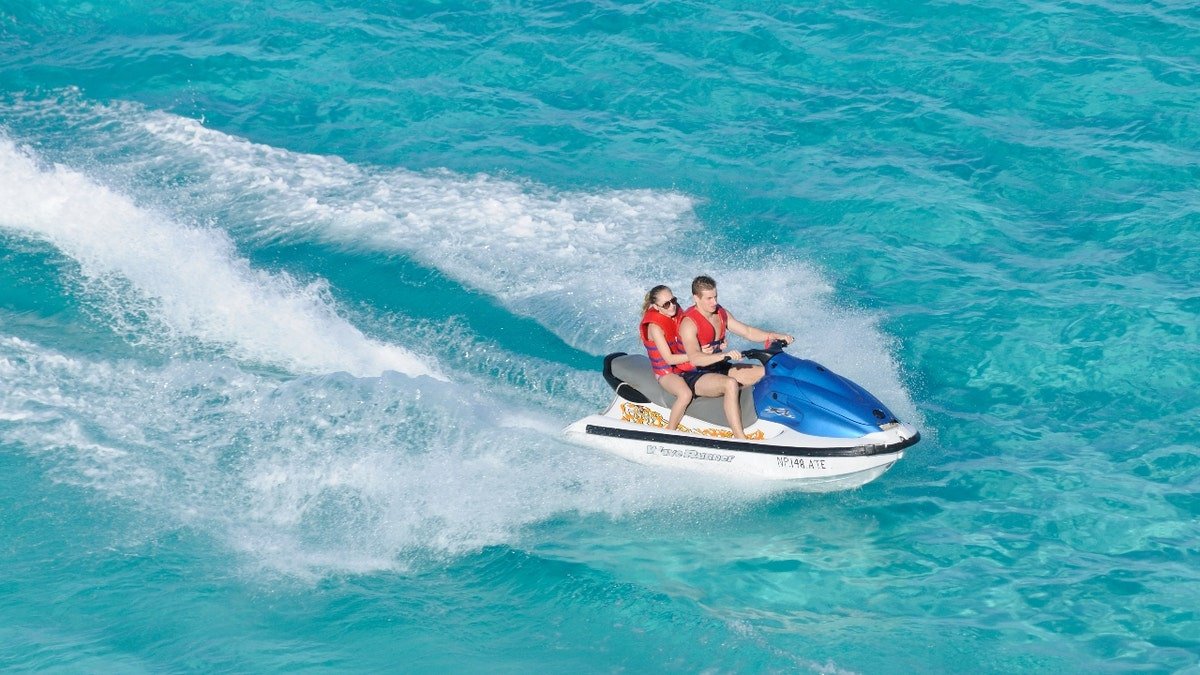 A man and woman riding a jet ski on blue water.