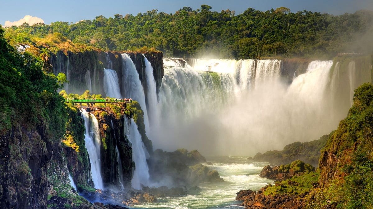 Panoramic view of Iguazu Falls cascading over rocky cliffs surrounded by lush rainforest.
