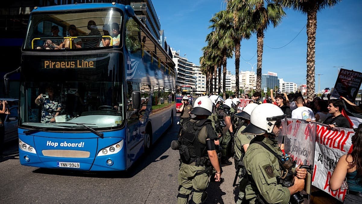 Israeli tourists traveling on buses past pro-Palestinian protestors and Greek security forces at Piraeus port