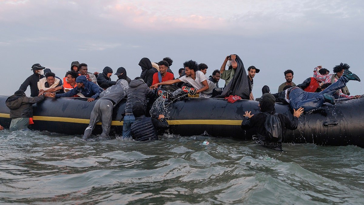 Migrants wading into water near Gravelines, France, with traffickers managing the scene
