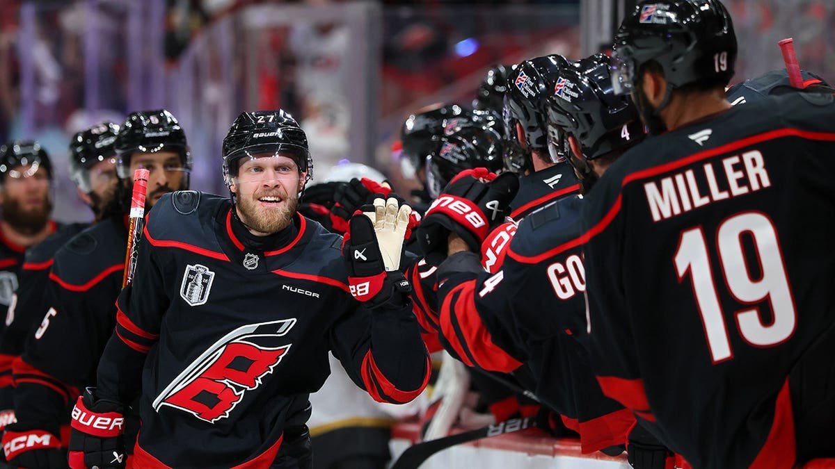 Nikolaj Ehlers celebrating with Carolina Hurricanes teammates after scoring a goal on ice rink.