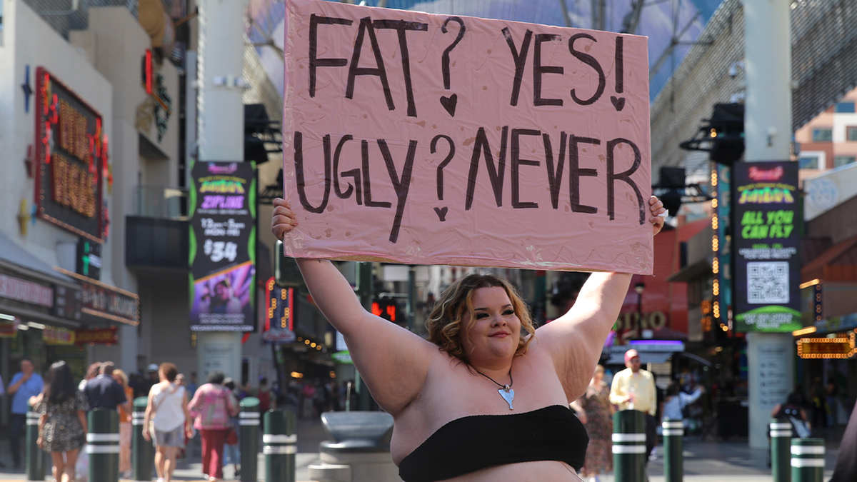 A Pearadise community member holds a body-positivity sign reading 