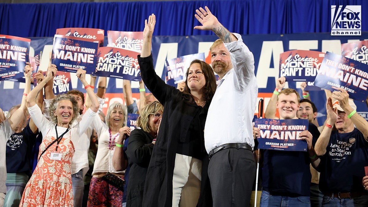 Graham Platner and his wife Amy Gertner waving at a watch party inside a YMCA in Blue Hill Maine.