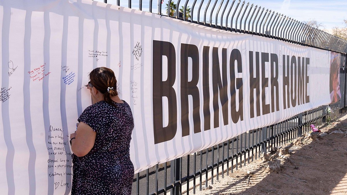 A well-wisher signing a banner with a photo of Nancy Guthrie outside KVOA newsroom in Tucson