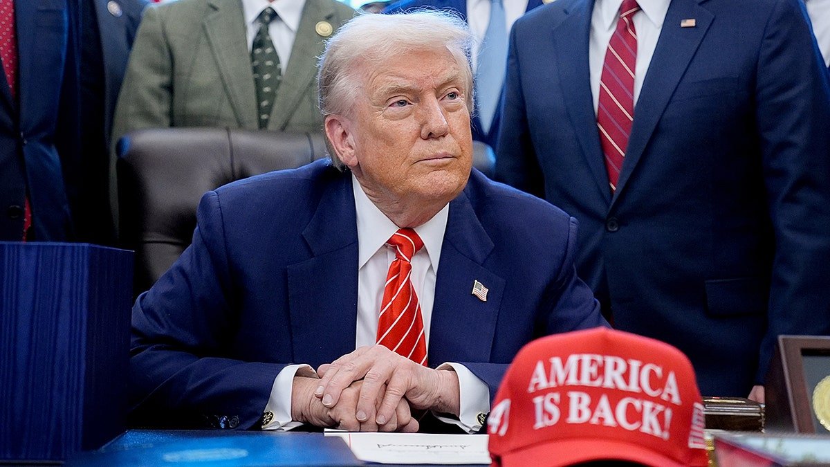 President Donald Trump sitting in the Oval Office wearing an America is Back hat.